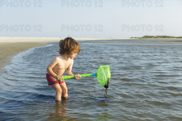Caucasian boy wading in ocean holding