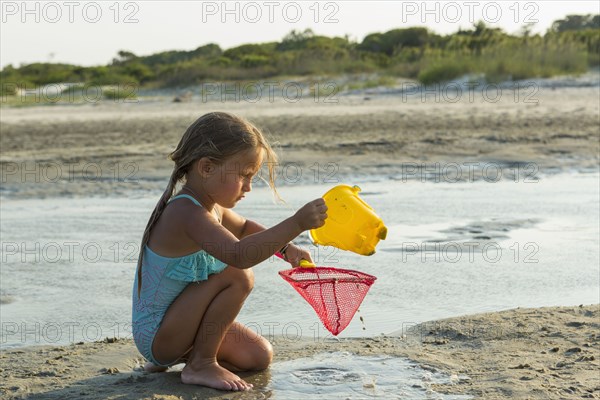 Caucasian girl kneeling on the beach pouring water into net