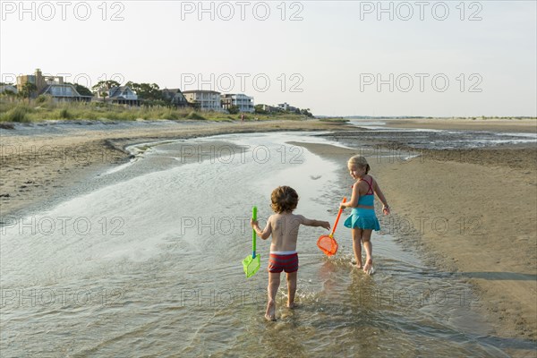 Caucasian brother and sister carrying nets on beach