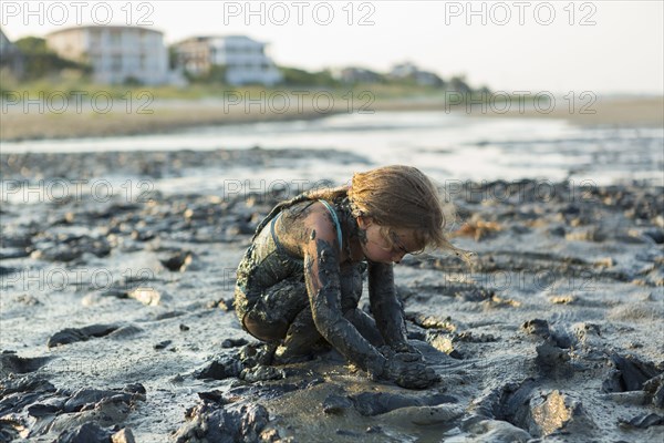 Caucasian girl covered in mud playing on beach