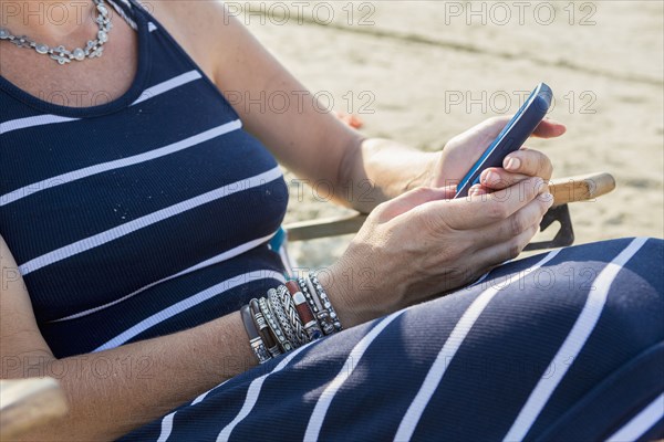 Caucasian woman sitting on the beach texting on cell phone