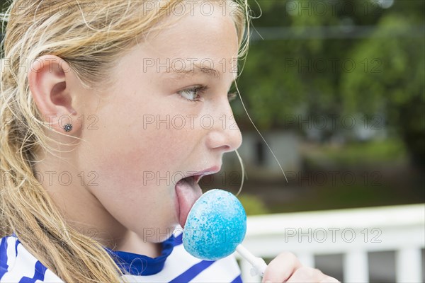 Tongue of Caucasian girl licking blue lollipop