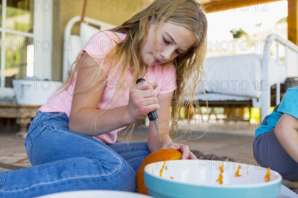 Caucasian girl sitting on floor carving pumpkin with knife