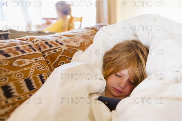 Caucasian boy laying in comforter texting on cell phone