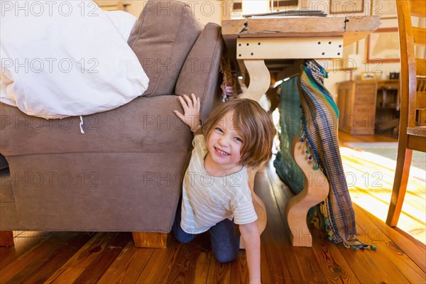 Caucasian boy crawling on floor between table and sofa