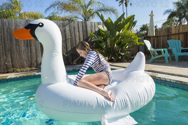 Caucasian girl sitting on inflatable swan in swimming pool