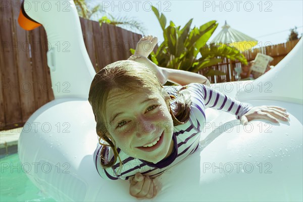 Caucasian girls laying on inflatable swan in swimming pool