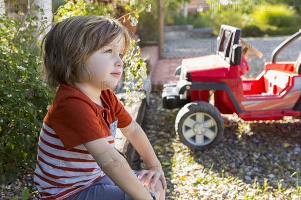 Pensive Caucasian boy sitting near toy car