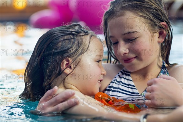 Caucasian girl holding brother in swimming pool