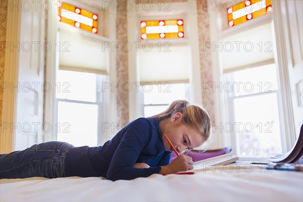 Caucasian girl laying on bed writing in notebook