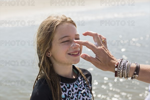 Caucasian mother applying sunblock to nose of daughter