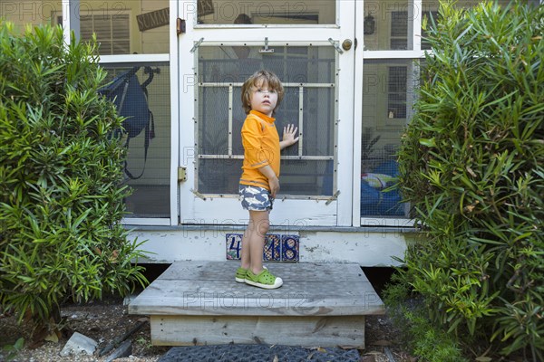 Curious Caucasian boy standing at screen door