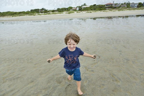 Caucasian boy running on beach carrying sand