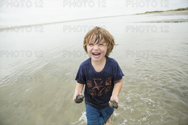 Caucasian boy waiting in ocean carrying sand