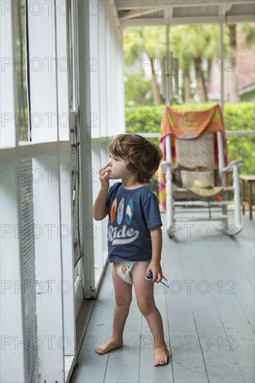 Curious Caucasian boy wearing diaper near screen door