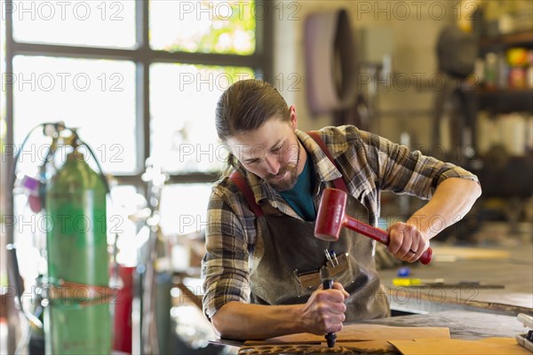 Caucasian man hammering leather in a workshop