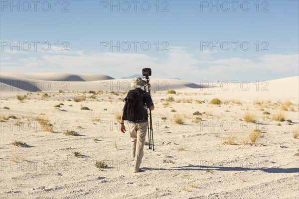 Rear view of Caucasian photographer carrying tripod in desert