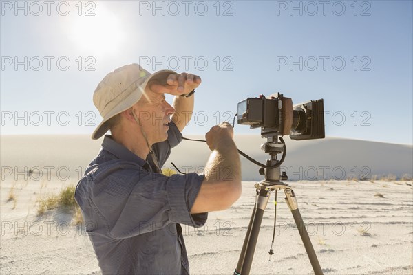 Caucasian photographer with tripod shielding eyes in desert
