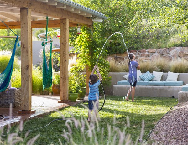 Caucasian boy spraying sister with hose in backyard