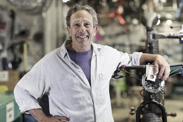 Portrait of smiling Caucasian man leaning on bicycle in shop