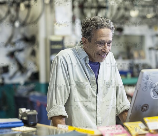 Smiling Caucasian man using computer in bicycle shop