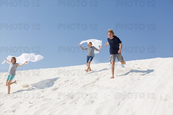 Caucasian boy and girls running on sand dune