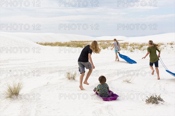 Caucasian boys and girls playing on sleds in sand
