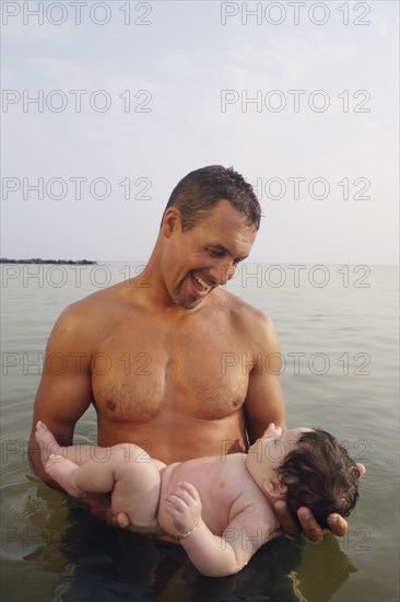 Mixed Race father holding baby in water