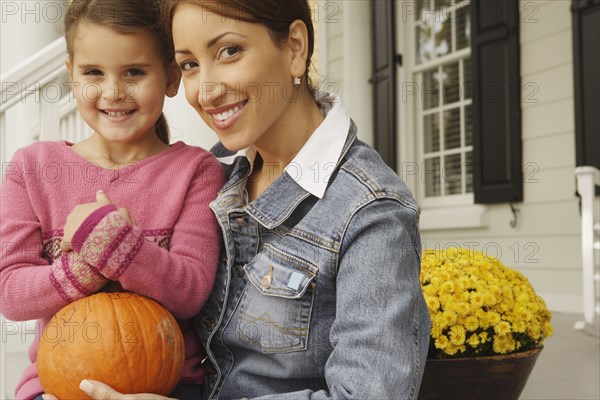 Hispanic mother and daughter holding pumpkin