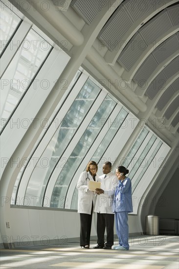 Multi-ethnic doctors and nurse reviewing medical chart in corridor