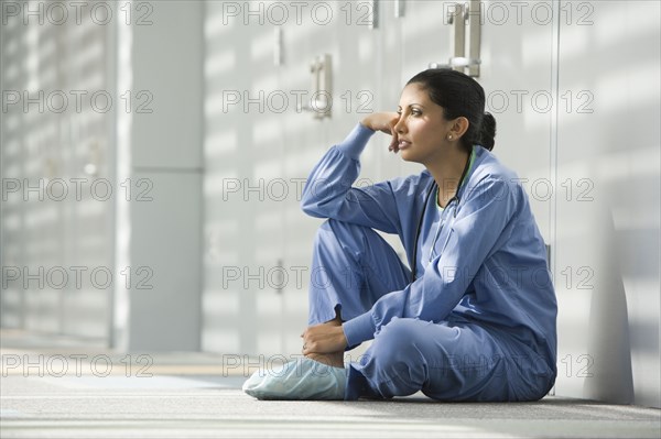 Hispanic nurse sitting on floor with head in hands