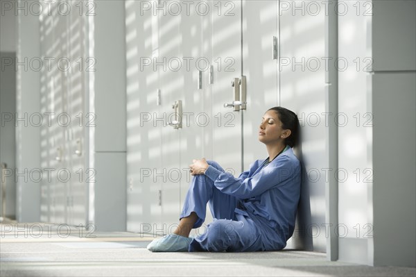 Hispanic nurse with eyes closed sitting on floor