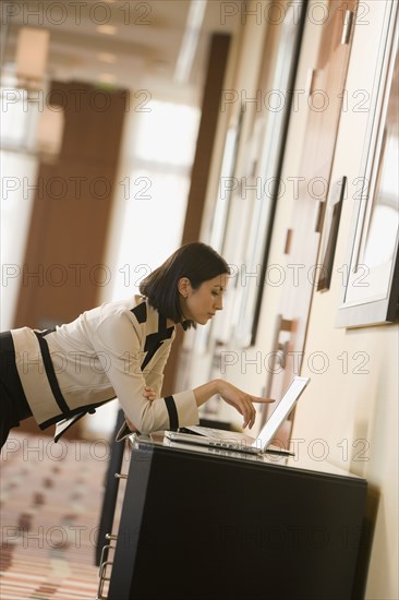 Mixed race businesswoman working on laptop in corridor