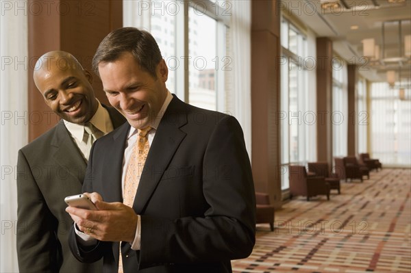 Multi-ethnic business people looking at cell phone in corridor