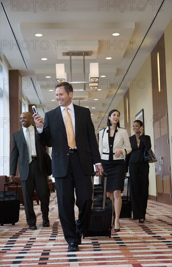 Multi-ethnic business people walking with suitcases down corridor