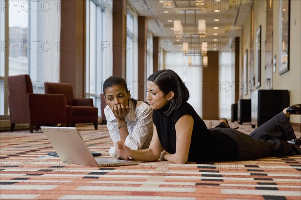 Multi-ethnic businesswomen laying on floor working on laptop