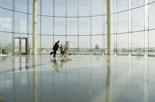 Businessman pushing businesswoman in rolling desk chair