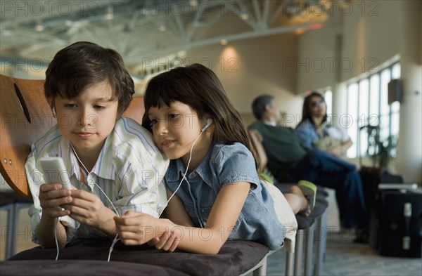 Hispanic brother and sister listening to mp3 player in airport