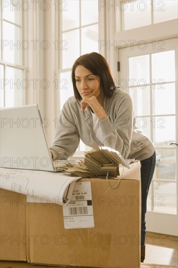 Hispanic woman using laptop on boxes