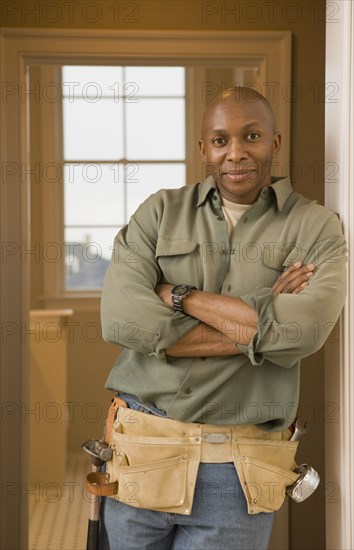 African man wearing tool belt with arms crossed