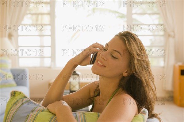Mixed race woman sitting on sofa in living room talking on cell phone