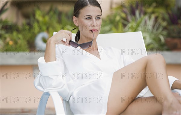 Mixed race woman in sunglasses sitting in lounge chair