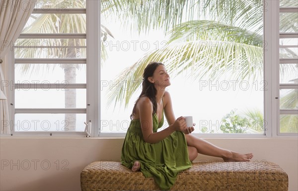 Mixed race woman drinking coffee near window