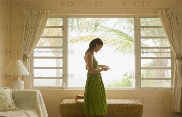 Mixed race woman looking at cell phone near window