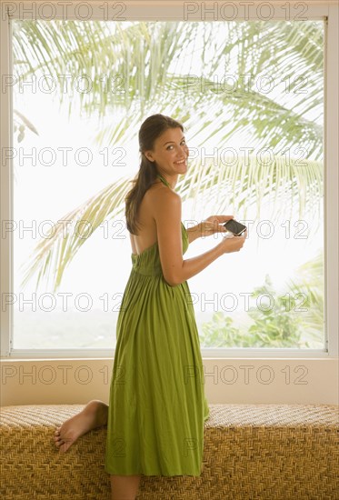 Mixed race woman holding cell phone near window