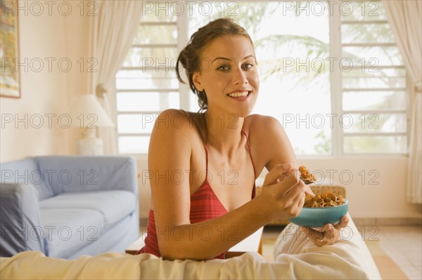 Mixed race woman eating cereal in living room