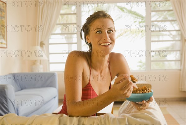 Mixed race woman eating cereal in living room