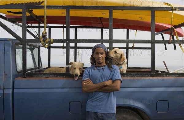 Hispanic man with dogs leaning against truck