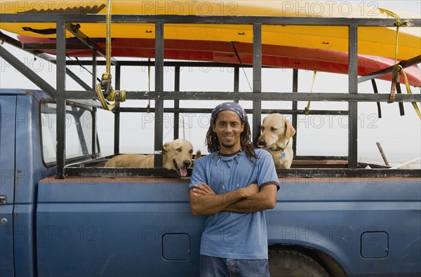 Hispanic man with dogs leaning against truck