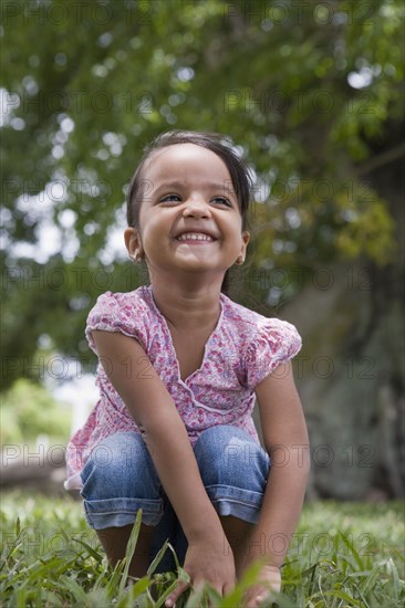 Grinning Hispanic preschool girl squatting in grass